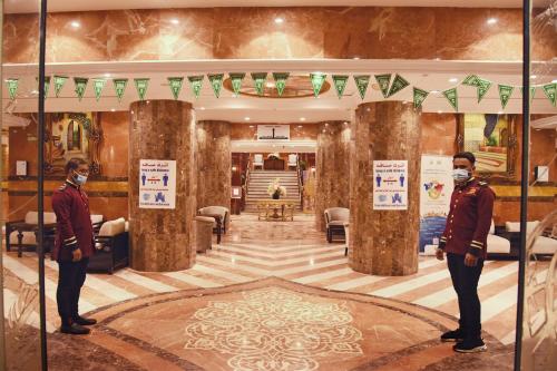 two men wearing face masks stand in a lobby at Al Andalus Palace 1 Hotel in Al Madinah