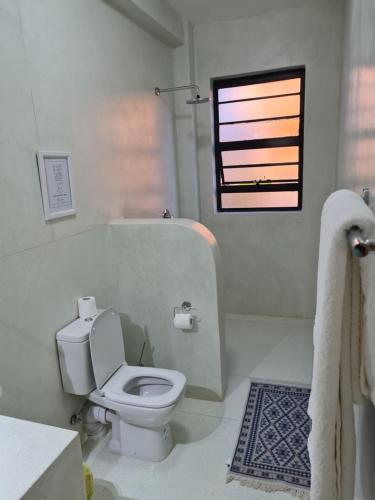 La salle de bains blanche est pourvue de toilettes et d'une fenêtre. dans l'établissement The Landing Nanyuki Cottages, à Nanyuki