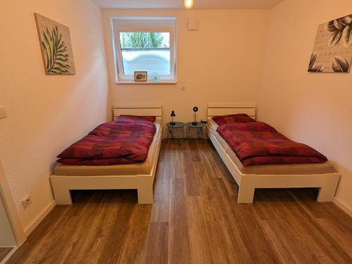 two beds in a room with wooden floors and a window at Moderne Neubau Ferienwohnung in Wiesbaden