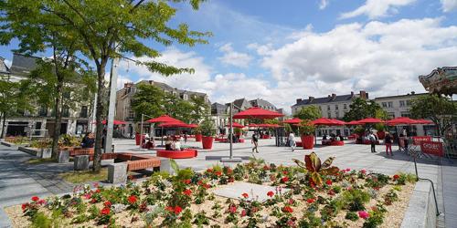 Une place avec des tables, des parasols rouges et des fleurs dans l'établissement Appartement Kennedy up, à Cholet