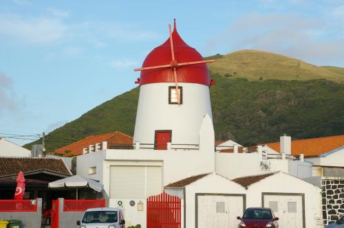 een rode en witte vuurtoren met een heuvel op de achtergrond bij Moinho Mó da Praia in Praia da Graciosa