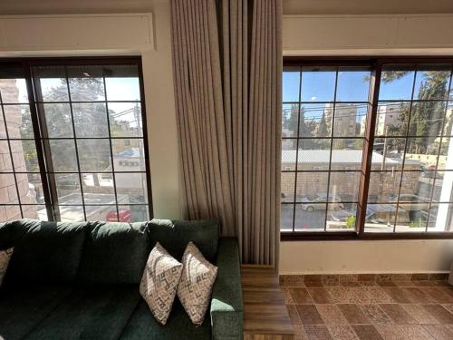 a living room with a green couch and large windows at 5/ Antica jabalal-lwebdeh in Amman