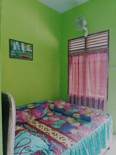a bed in a green room with a window at Penginapan Ana Indah in Borobudur