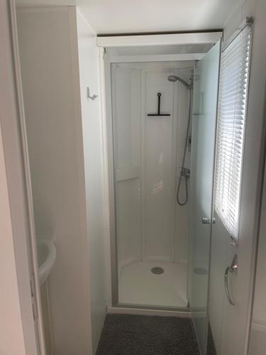 ein weißes Bad mit einer Dusche und einer Glastür in der Unterkunft Mobil-home Confort TV CLIM Narbonne-Plage in Narbonne-Plage