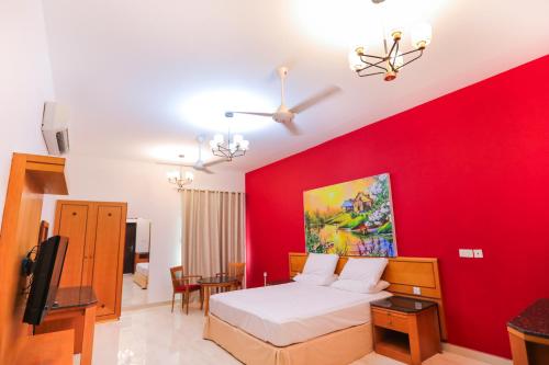 a bedroom with a red wall with a bed and a tv at Bahjat Al Azaiba Villa in Muscat