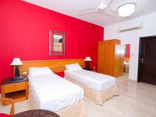 two beds in a room with a red wall at Bahjat Al Azaiba Villa in Muscat