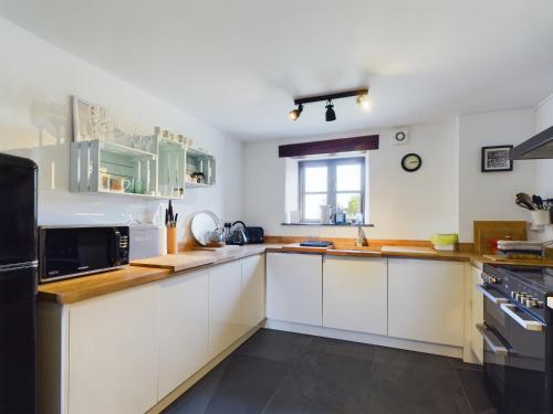 una cocina con armarios blancos y electrodomésticos negros en Cosy Stone Cottage in Llanarthney nr Carmarthen, en Llanarthney