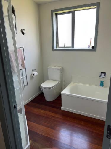 a bathroom with a tub and a toilet and a window at Hosts on the Coast - Reel Escape on Banks in Cooks Beach