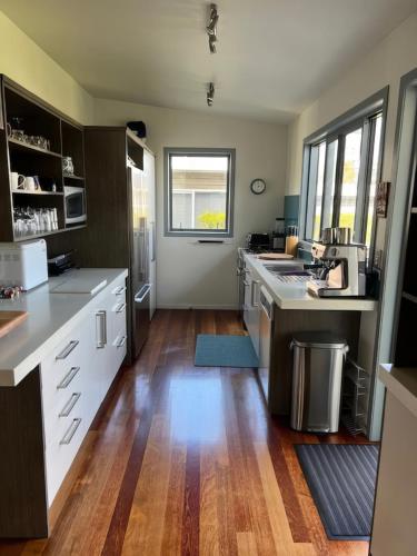 a large kitchen with wooden floors and white cabinets at Hosts on the Coast - Reel Escape on Banks in Cooks Beach