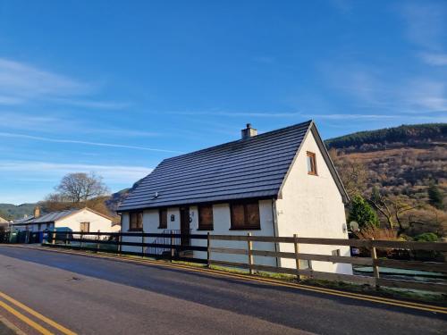 a white house with a black roof on the side of a road at Wilmar Lodge in Arrochar