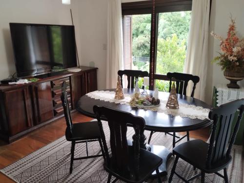 een eetkamer met een tafel met stoelen en een televisie bij Casa aconchegante Gramado em local tranquilo- 5 km do centro locação temporada in Gramado