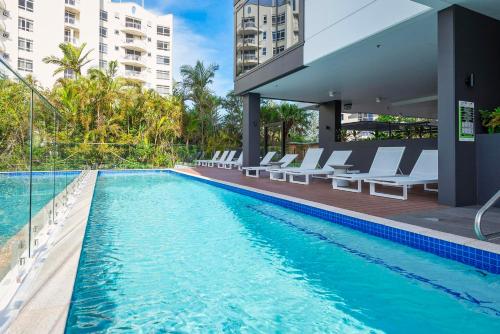 a swimming pool with lounge chairs next to a building at Breathtaking Burleigh Beach Abode in Gold Coast