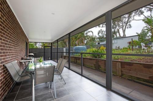 an outdoor patio with a glass table and chairs at Tangerine - Pet Friendly - 3 Mins Walk to Beach in Sanctuary Point