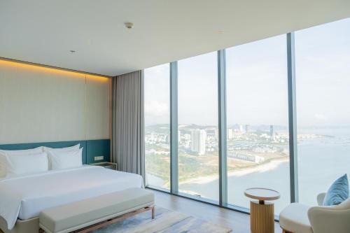 a bedroom with a bed and large windows at A La Carte Ha Long Bay Managed by TASECO in Ha Long
