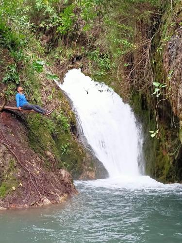 a man sitting on a log in front of a waterfall at Hacienda Aventuras en el Paraíso in Quito