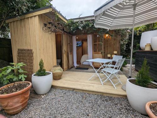 een houten terras met een tafel en een parasol bij Piccola Casa Fiorita in Mount Maunganui