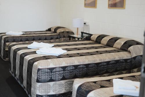 three beds in a hotel room with towels on them at Porky's Motel Rockhampton in Rockhampton