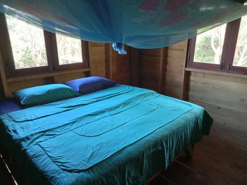 a bedroom with a bed with blue sheets and windows at Fandee Island - Secret Private House - Tad Lo Bolaven Loop Pakse in Ban Kiangtat