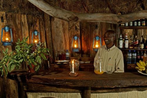 un hombre sentado en un bar con una mesa en Crater Forest Tented Lodge en Karatu