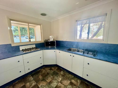 a kitchen with white cabinets and a sink and two windows at West View Caravanpark in Dubbo