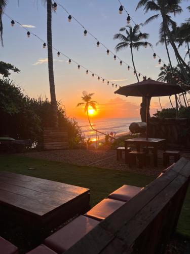 a sunset on the beach with a bench and an umbrella at Top Secret Beach Hotel in Matara