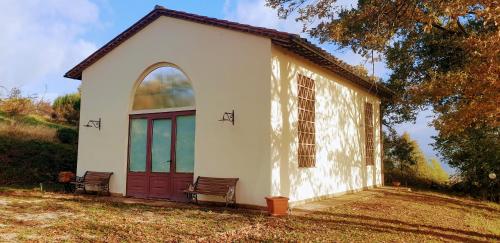 a small white chapel with a red door and two benches at Alto Locandieri in Montebagnolo