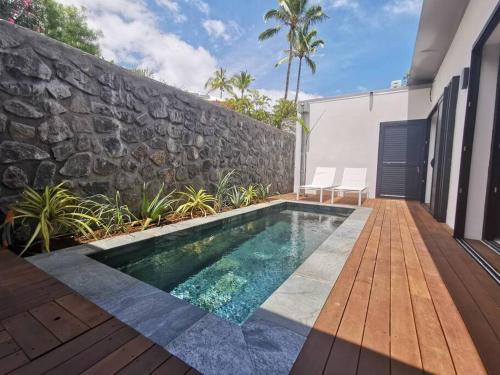 a swimming pool in front of a stone wall at SUMMER COSY - Villa classée 4 étoiles - 2 suites avec piscine chauffée et jacuzzi intégré idéalement située Chemin Summer in Saint-Gilles les Bains