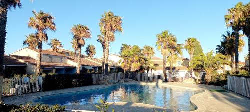 uma piscina num quintal com palmeiras em Petit pavillon pour 6 personnes dans une résidence avec piscine em Valras-Plage