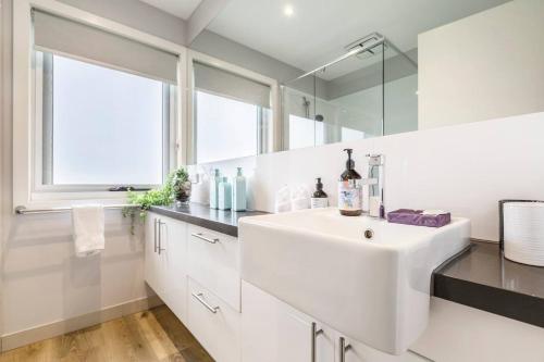 a white bathroom with a sink and a mirror at 'Caulfield Charm' Chic Inner-City Refuge in Melbourne