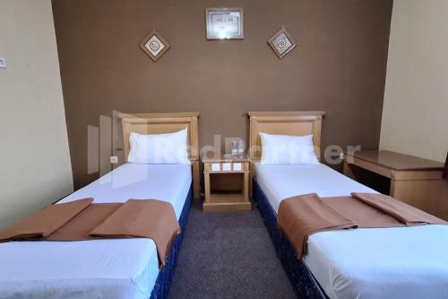 two beds in a small room with two tables at Hotel Graha Muslim RedPartner in Bukittinggi