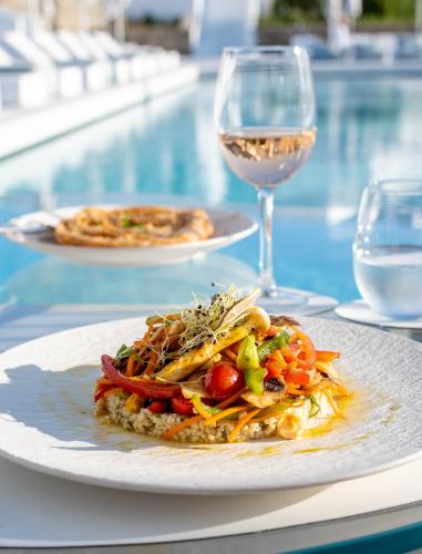 a plate of food on a table with a glass of wine at Mykonos Bay Resort & Villas in Mýkonos City