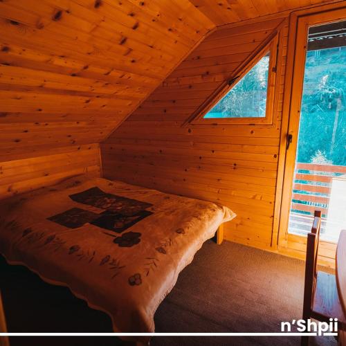 a bed in a log cabin with a window at N'SHPII VILLA in Peje