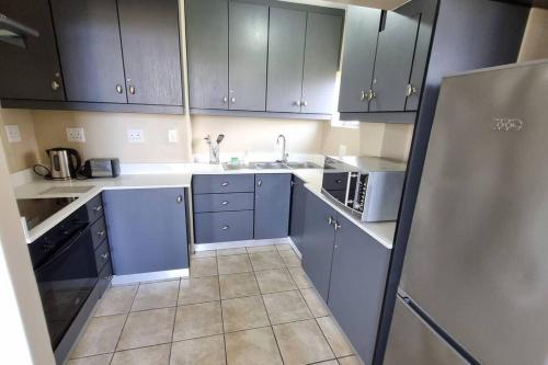 a kitchen with blue cabinets and a sink and a refrigerator at Upmarket Beach Flat, Free WiFi & DisneyPlus in Durban