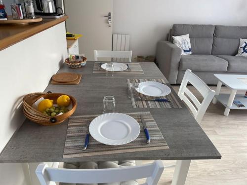 - une table à manger avec des assiettes et un bol de fruits dans l'établissement Appartement le Kingsbridge, à Isigny-sur-Mer