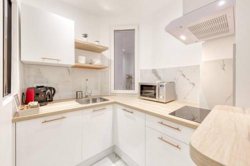 une cuisine blanche avec des armoires blanches et un micro-ondes dans l'établissement Le Paisible Parisien à 3 minutes du métro, à Vincennes