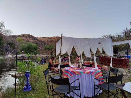 a tent with a table and chairs next to a river at The Jungle Lust in Kumbhalgarh