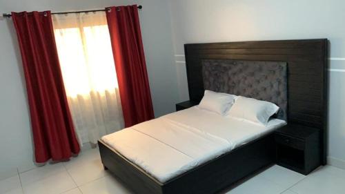 1 dormitorio con 1 cama con cortinas rojas y ventana en PNHouse Anguissa A2, en Yaoundé