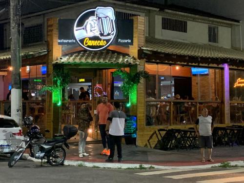 a group of people standing outside of a bar at night at Apartamento Praia do Morro - Guarapari in Guarapari