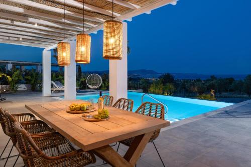 a wooden table and chairs on a patio with a pool at Sunset Hill Villa Rhodes in Gennadi