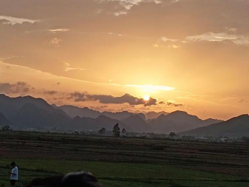 a sunset over a field with mountains in the background at Palafita Bungalow in Phong Nha