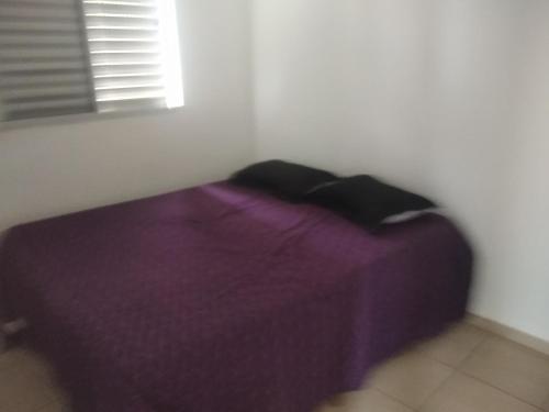 a purple bed in a white room with a window at Apartamento bem localizado in Franca