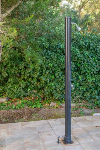 a black pole on a sidewalk in front of a bush at Pomeres 9 in Sa Coma
