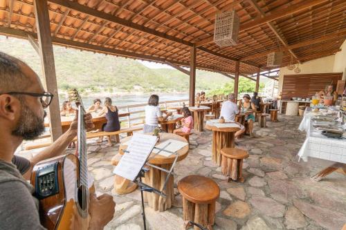 Een man die gitaar speelt in een restaurant met mensen aan tafel. bij Pousada Porto de Piranhas in Piranhas