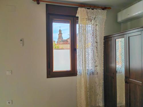 a window with curtains and a view of a church at Casa Rural Teralba 2 in La Calzada de Oropesa