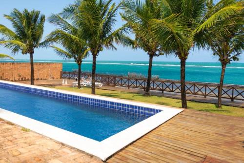 a swimming pool with palm trees and the ocean at Villa Patara in Marechal Deodoro