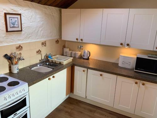 a kitchen with white cabinets and a sink and a stove at Cider Cottage - 3 Bedroom - Onsite Parking in Sidmouth