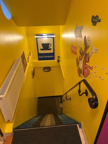 a yellow room with a stairs with a sign on the wall at Very Bad Hootel in Kaunas
