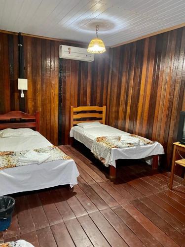 two beds in a room with wooden walls at Pousada Encantos da Amazônia in Alter do Chao