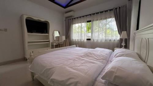 ein weißes Schlafzimmer mit einem großen Bett und einem Fenster in der Unterkunft Cozy Villa Tai in Na Jomtien