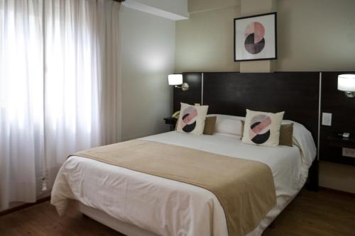 1 dormitorio con 1 cama grande con sábanas y almohadas blancas en Hotel San Carlos en General Juan Madariaga